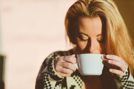 Woman wearing a sweater drinking a cup of coffee